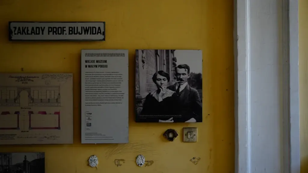 Historyczne tablice i fotografie na żółtej ścianie w polskim muzeum.