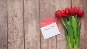 Odręcznie napisana notatka z podziękowaniem, koperta i czerwone tulipany na drewnianym stole.